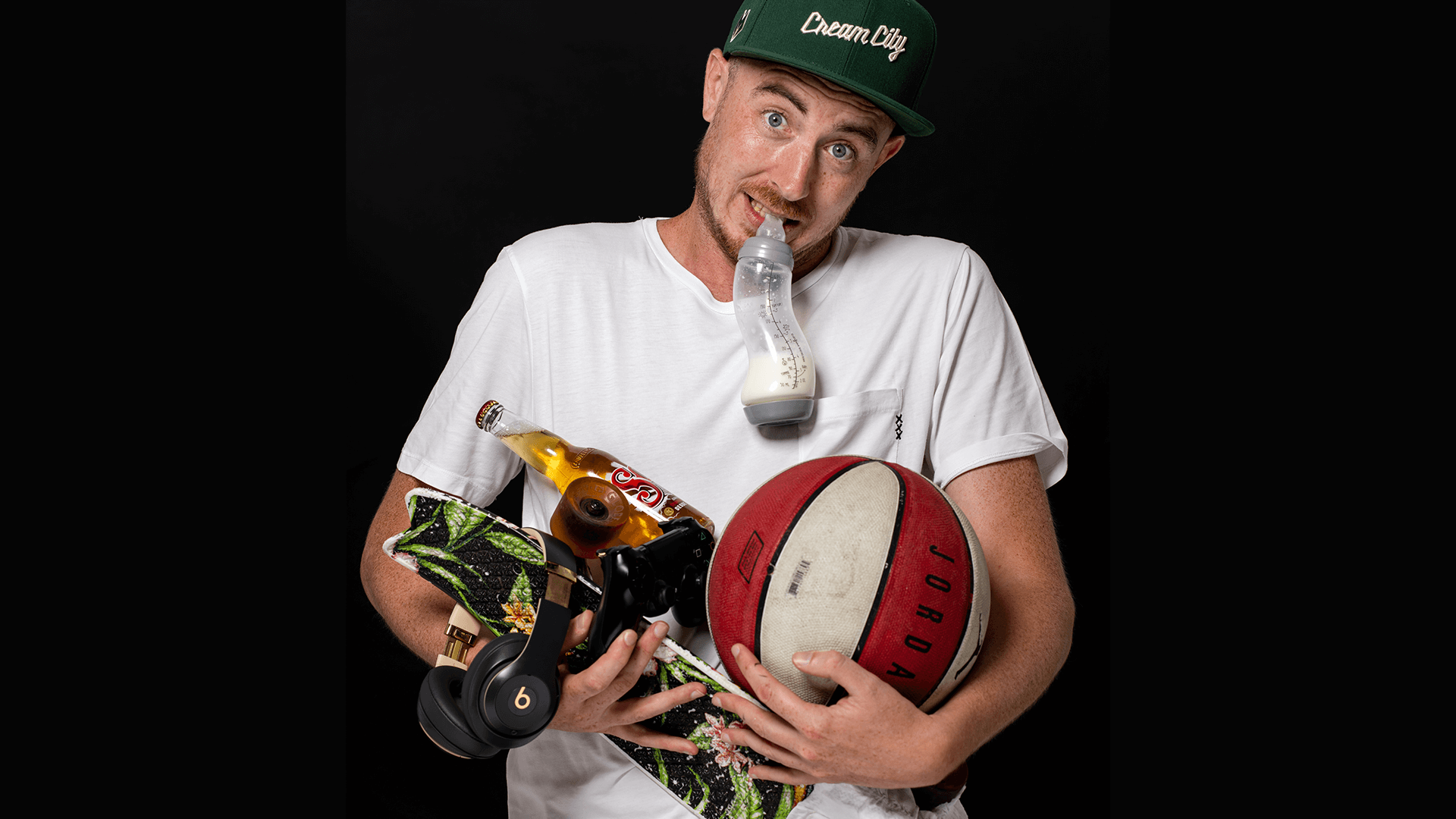 Davey Turnhout met veel attributen in zijn handen, zoals een basketbal, babyfles en skateboard.