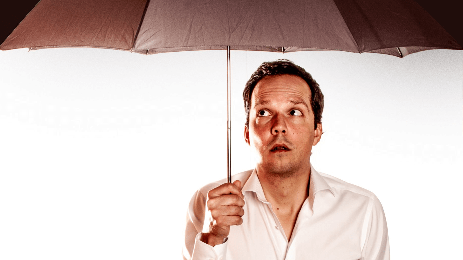 Peter van Ewijk kijkt geschrokken onder een bruine paraplu